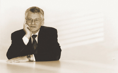 Douglas R. Carmichael sitting at a desk, leaning on his elbow.
